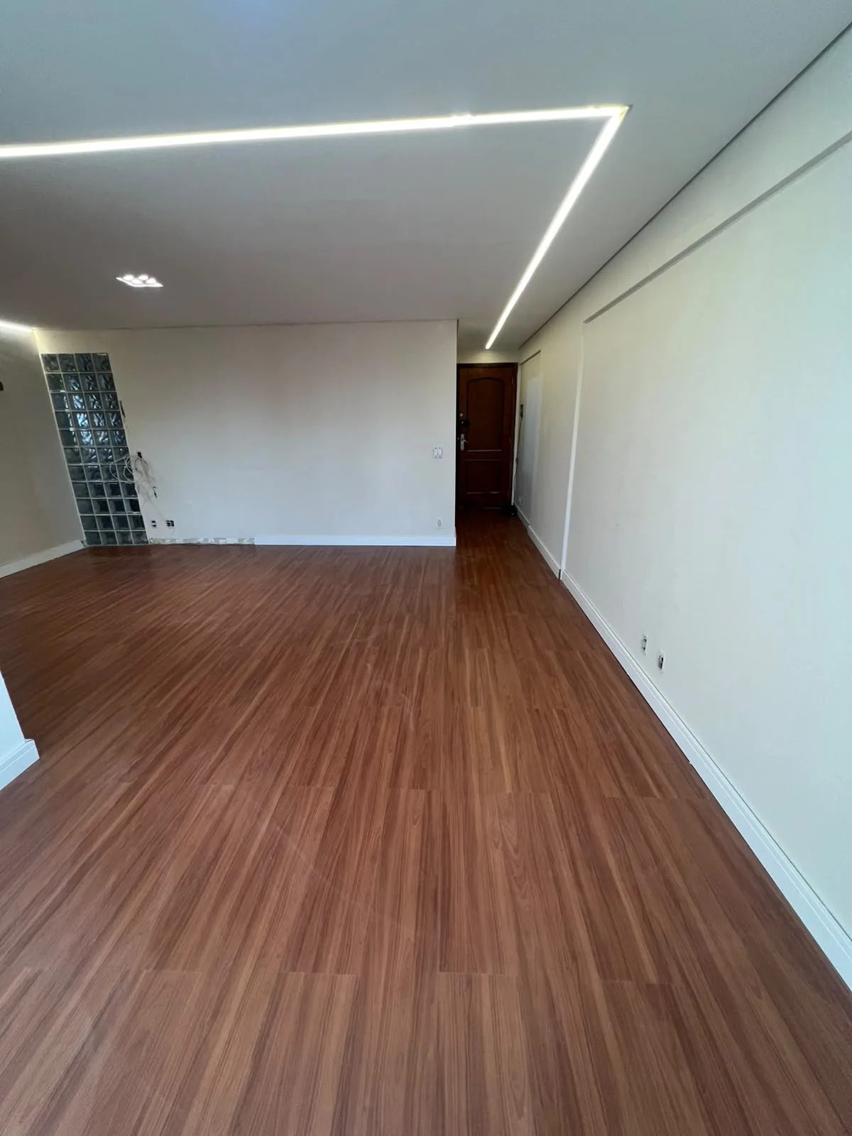 Depois: sala de apartamento reformada com piso de madeira e iluminação embutida em São Paulo